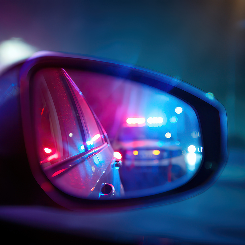Police lights reflected in a driver's side mirror